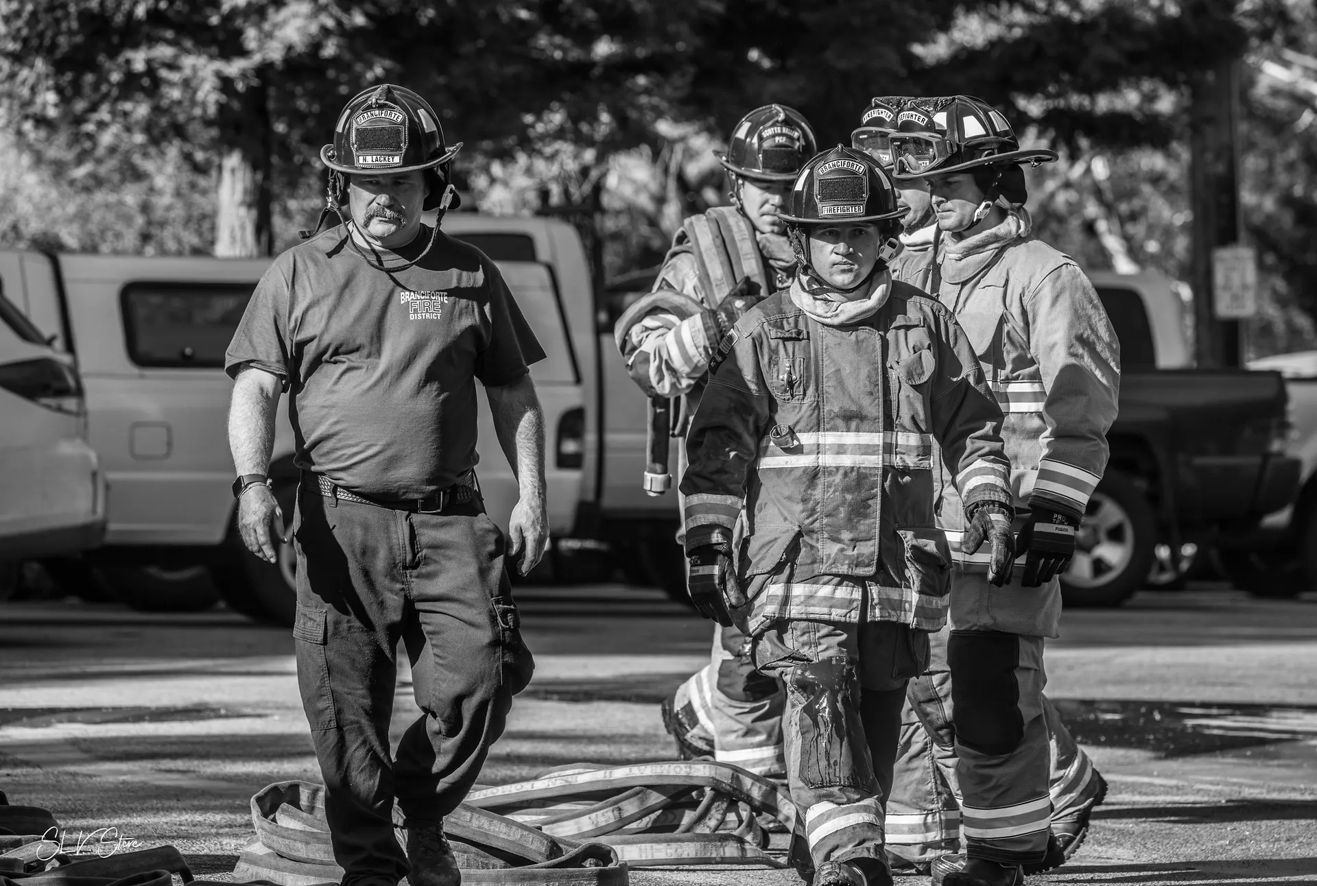 Firefihter climbing ladder that is leaning against fire station. Another firefighter is supporting the ladder while two other firefighters observe.